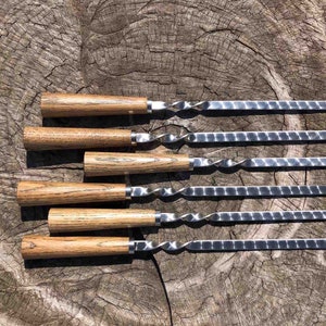 May include: Set of six wooden handled skewers with twisted metal shafts. The skewers are arranged in a row on a wooden surface.