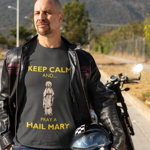 May include: A black t-shirt with a yellow graphic that says "Keep Calm and... Pray a Hail Mary". The graphic also features a depiction of the Virgin Mary.
