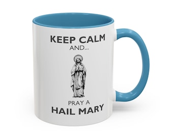 Könnte beinhalten: Weiße Keramiktasse mit hellblauem Rand und Henkel. Die Tasse zeigt ein Schwarzweißbild der Jungfrau Maria und den Text "Keep Calm and... Pray a Hail Mary".