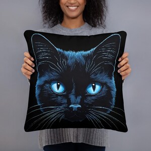 May include: Black throw pillow featuring a detailed illustration of a black cat's face with striking blue eyes. The cat's fur is depicted with intricate detail, and the background is solid black. A decorative accent for any room.