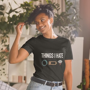 May include: Black t-shirt with the text "THINGS I HATE" and graphics of a loading circle, a low battery, and a Wi-Fi signal. The shirt is worn by a person.