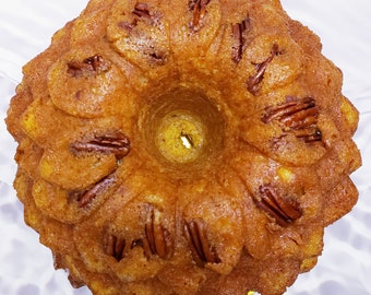 以下が含まれることがあります： ペカンナッツがトッピングされた、黄金色のバンドケーキ。ケーキはバンド型で、サーブする準備ができています。