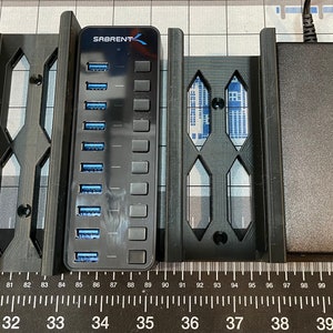 May include: A black USB hub with 10 ports, a power adapter, and two black brackets. The hub is labeled "SABRENT" and has blue USB ports. The brackets have an open geometric design.