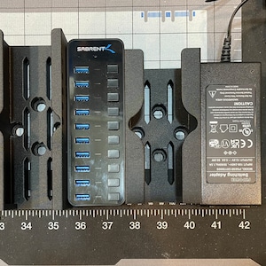 May include: Black USB hub with the brand name "SABRENT" and a power adapter. The hub has multiple USB ports with blue inserts. The power adapter has a warning label and technical specifications.