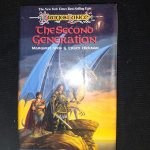 May include: A paperback book titled "The Second Generation" by Margaret Weis & Tracy Hickman. The cover features a fantasy illustration of a warrior, a dragon, and a young person with a cape. The book is part of the Dragonlance Saga.
