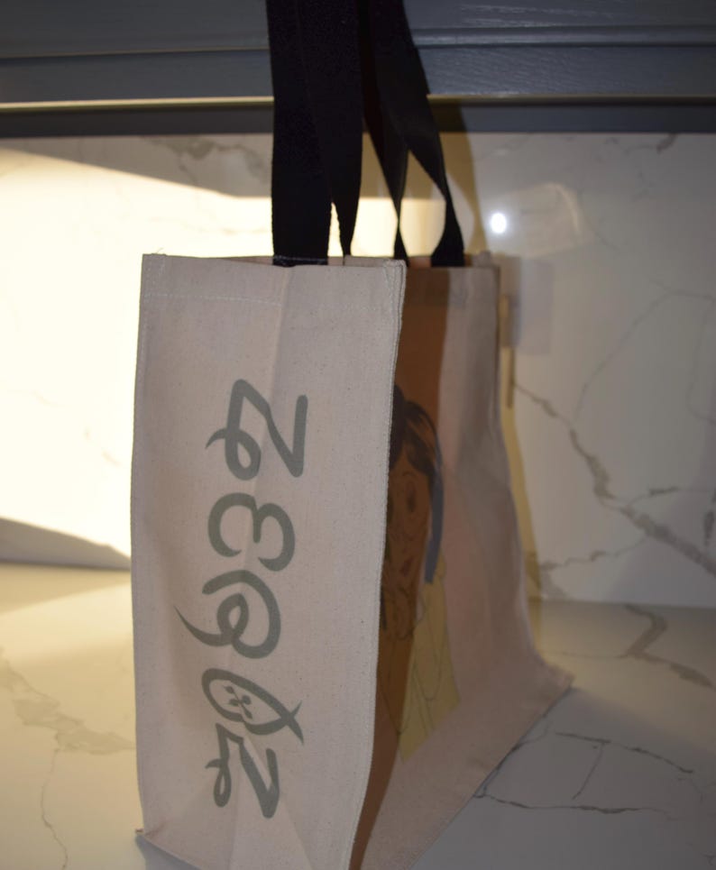 May include: A beige canvas tote bag with black handles. The bag has a green design on the front that says "Zegna 2023".