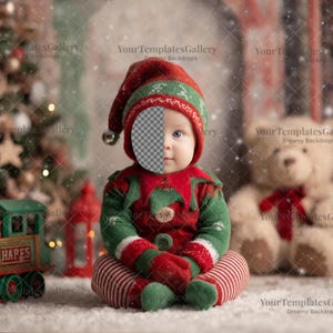 May include: A baby dressed in a red and green elf outfit with a matching hat and mittens sits in front of a Christmas tree and a teddy bear. A toy train with the word "HAPES" is in the foreground.