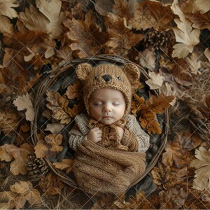 May include: A newborn baby wearing a brown knitted bear hat and a brown knitted swaddle, sleeping in a basket surrounded by autumn leaves.