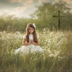 May include: A young girl in a white dress with a flower in her hair kneels in a field of wildflowers. A wooden cross stands in the background. The scene is bathed in soft, natural light, creating a serene and peaceful atmosphere.