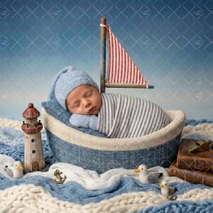 May include: A newborn baby sleeps peacefully in a nautical-themed boat. The baby is wrapped in a striped blanket and wears a blue hat and mittens. A miniature sailboat with a red and white striped sail is nearby, along with a lighthouse and other nautical decorations.