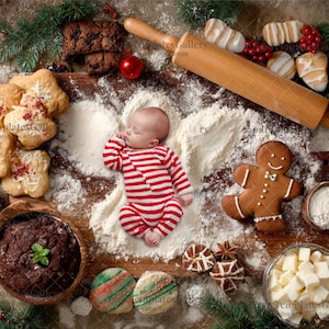 May include: A newborn baby in a red and white striped onesie lies on a wooden surface surrounded by flour, cookies, and baking supplies. A gingerbread man, rolling pin, and chocolate cake are also visible.