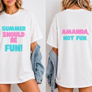 Può includere: T-shirt bianco con la scritta "SUMMER SHOULD BE FUN!" in blu e rosa sul davanti. Il retro della maglietta dice "AMANDA, NOT FUN." in rosa e blu. La maglietta è indossata con una giacca di jeans.