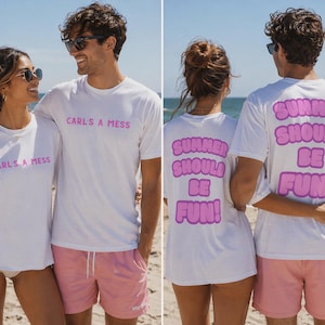 May include: White t-shirts with pink text reading "CARL'S A MESS" on the front and "SUMMER SHOULD BE FUN!" on the back. The models wear pink shorts and sunglasses, standing on a sandy beach with the sea in the background.
