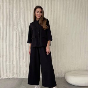 May include: A black button-up shirt and wide-leg pants set. The shirt has a mock neck and long sleeves. The pants have a wide leg and a relaxed fit.