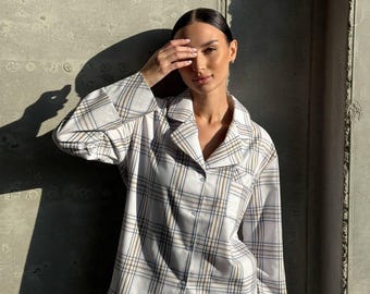 May include: A light-colored plaid pajama set. The set includes a button-down shirt with a collar and matching pants. The plaid pattern features white, blue, and brown lines. The pajamas are made of a soft, comfortable material.