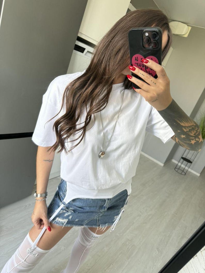 May include: White short-sleeved t-shirt paired with a denim mini-skirt. The skirt has distressed details and white suspender straps. The outfit is accessorized with a silver necklace and white thigh-high stockings.