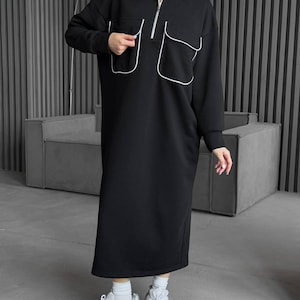 May include: A black long-sleeved dress with white piping detail. The dress has a mock neck and a zipper closure. The dress has two large pockets on the front.