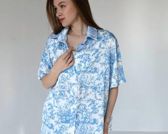 Puede incluir: Conjunto de pijama de dos piezas con un estampado de toile de Jouy azul y blanco. El conjunto incluye una camisa de manga corta con botones y pantalones cortos a juego. La tela tiene un aspecto suave y fluido.
