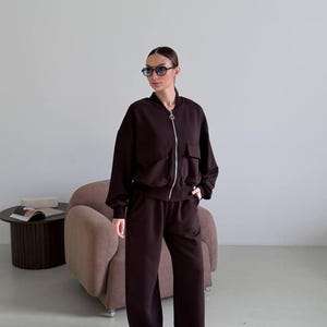 Conjunto feminino marrom chocolate de duas peças, composto por jaqueta bomber oversized e calça pantalona em malha felpuda, estilo minimalista para relaxar.