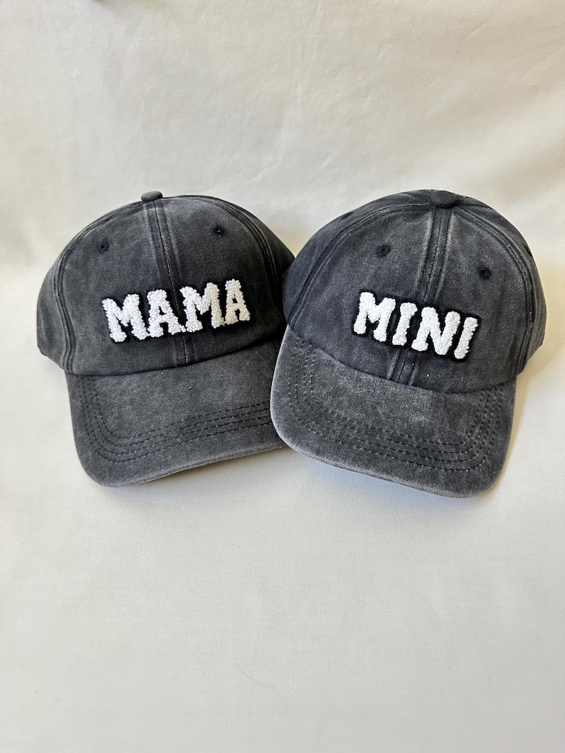 May include: Two black denim baseball caps with white embroidered text. One cap says "MAMA" and the other says "MINI".