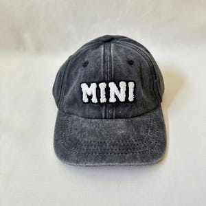 May include: A black denim baseball cap with white embroidered text that reads "MINI".