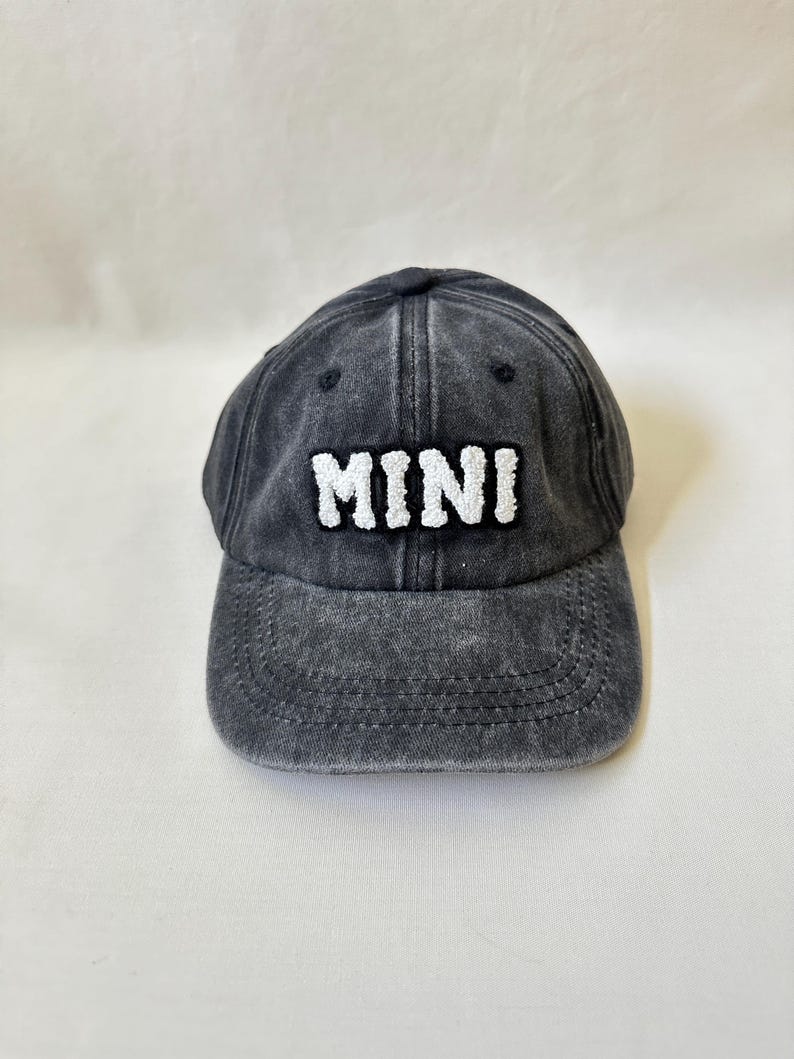 May include: A black denim baseball cap with white embroidered text that reads "MINI".