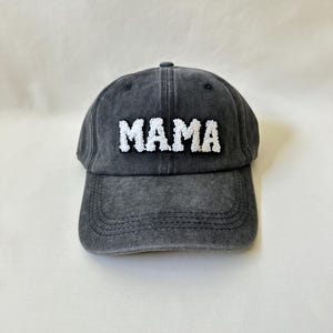 May include: A black denim baseball cap with white embroidered text that reads "MAMA".