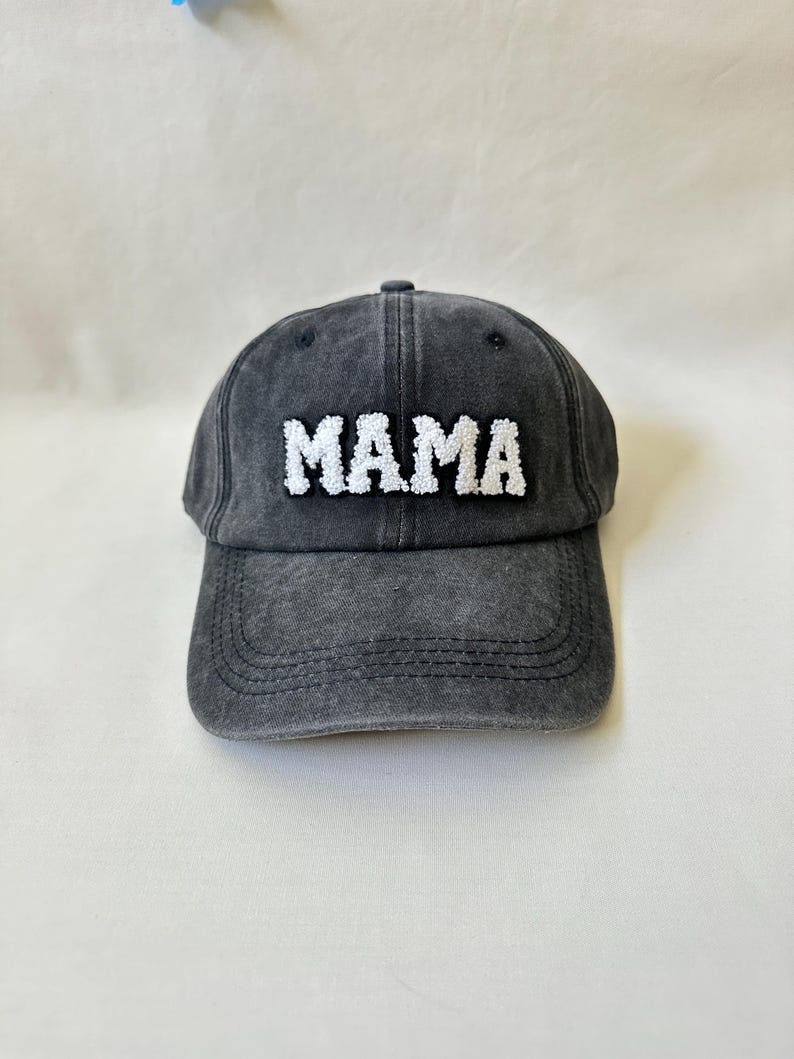 May include: A black denim baseball cap with white embroidered text that reads "MAMA".