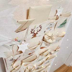 Beiger Adventskalender Leinen-Stoff zum Befüllen, für Kinder und Erwachsene, zum an die Wand hängen mit Kordel und Holzstange, Ziermotive, Rentier, Weihnachtsmann, Weihnachten, Dekoration für Geschenke, beige, rot, grün, braun, blau