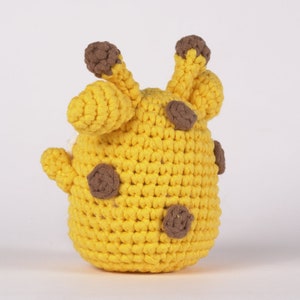 May include: A yellow crocheted giraffe toy with brown spots. The giraffe has a round body and a long neck with a small head.