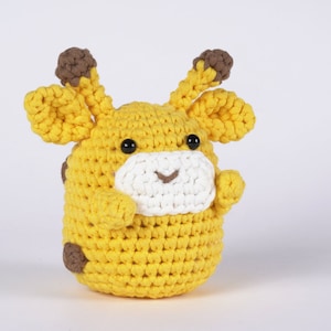 May include: A crocheted stuffed giraffe toy with brown ears and spots. The giraffe is yellow with a white face and black eyes.