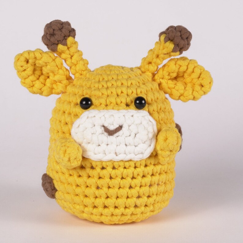 May include: A crocheted stuffed giraffe toy with brown ears, yellow fur, and a white face with black eyes and a smile.