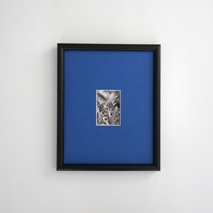 May include: A framed artwork featuring a small black and white illustration centered on a vibrant blue background. The frame is black, and the artwork appears to be a detailed drawing of plants or foliage. The overall aesthetic is minimalist and modern.