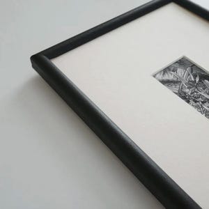May include: A framed black and white print featuring a detailed illustration. The artwork is set within a black wooden frame, creating a classic and elegant presentation. The print is centered on a white mat.