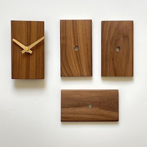 Könnte beinhalten: Eine Holzuhr mit goldenen Zeigern und einem schlichten Design. Die Uhr besteht aus vier separaten Holzstücken, jedes mit einem Loch in der Mitte. Die Uhr ist an einer weißen Wand montiert.