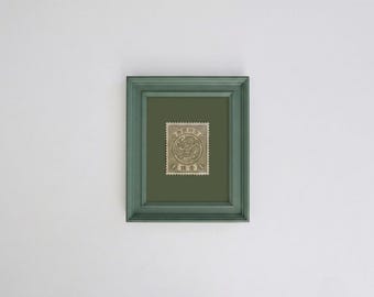Könnte beinhalten: Ein rechteckiger salbeigrüner Bilderrahmen mit einer alten Briefmarke, die ein zentrales kreisförmiges Design mit einer Drachenillustration und japanischen Schriftzeichen zeigt, auf einem passenden salbeigrünen Passepartout.