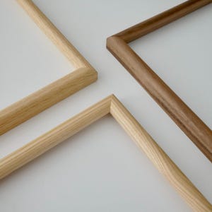 Pode incluir: Close-up dos cantos de três molduras de madeira. Duas são de cor clara e uma é castanha mais escura. As molduras são feitas de madeira e têm um design simples e moderno. Os cantos são precisamente unidos.