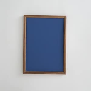 Pode incluir: Uma moldura retangular de madeira com interior azul escuro. A moldura tem um acabamento castanho quente e está montada numa parede branca. A moldura está vazia, pronta para uma foto ou obra de arte.