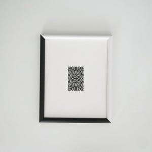 Könnte beinhalten: Ein gerahmtes Kunstwerk mit einem schwarz-weißen geometrischen Muster. Das Kunstwerk ist auf einem weißen Hintergrund in einem schwarz-weißen Rahmen zentriert. Das Muster ist ein sich wiederholendes Design aus ineinandergreifenden Formen.