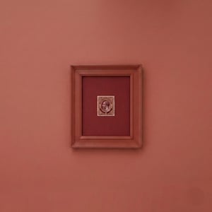 May include: A rectangular wooden frame with a dark red matting containing a single vintage postage stamp. The stamp features a portrait of a monarch in profile, surrounded by ornate decorative borders and text in a deep brown color.