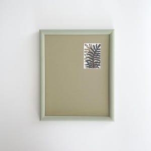 May include: A framed print with a botanical illustration. The frame is a pale green, and the print has a beige background with a rectangular botanical image in the upper right corner. The botanical image has dark green and brown details.