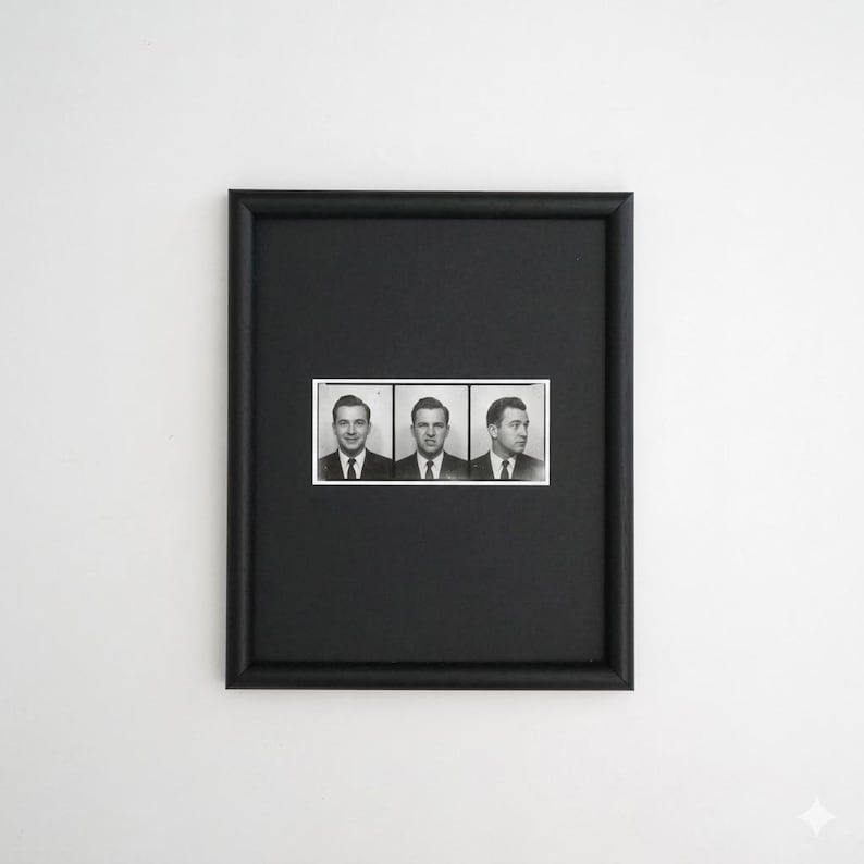 May include: Black framed artwork featuring three black and white portrait photographs of men in suits. The portraits are arranged horizontally within a white rectangular border. The frame is a simple, solid black.