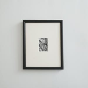 May include: A framed black and white botanical print. The artwork features a detailed illustration of plants and foliage. The print is set within a white mat and a black frame, creating a classic and elegant presentation.