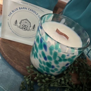 Puede incluir: Una vela de vidrio con un interior de cera blanca y una mecha de madera. El vidrio est&aacute; decorado con manchas azules y turquesas. Se ve una caja con el texto "THE BLUE BARN CANDLE CO.".