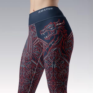 May include: Dark navy blue leggings featuring a high waistband with the white text FJORD & FORME. The fabric displays a detailed red and silver graphic print of a dragon head and intricate Celtic-inspired knotwork patterns across the legs.