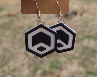 May include: A pair of black and white geometric earrings with gold hooks. The earrings are shaped like hexagons with a black and white geometric design.