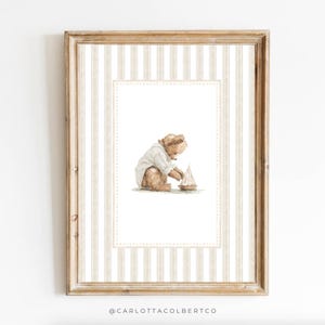 Puede incluir: Una impresión en acuarela enmarcada que presenta un oso de peluche con una camisa blanca jugando con un pequeño velero. La obra de arte tiene una paleta de colores neutros con un fondo a rayas beige y blanco y un borde decorativo. El marco es de color marrón claro.