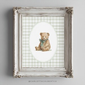 May include: A framed print featuring a watercolor illustration of a teddy bear with a green bow. The bear is set against a green and white gingham pattern within an oval frame. The frame is white with ornate detailing.