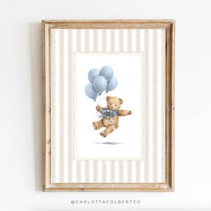 K&ouml;nnte beinhalten: Ein gerahmter Druck mit einer Aquarellillustration eines Teddyb&auml;ren, der mit blauen Luftballons schwebt. Der B&auml;r hat ein blaues Band und ist vor einem gestreiften Hintergrund platziert. Der Rahmen ist hellbraun.