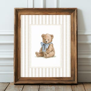 May include: A framed print featuring a watercolor illustration of a teddy bear with a blue ribbon. The bear is light brown, set against a striped background in a wooden frame. The artwork is a charming piece of nursery decor.